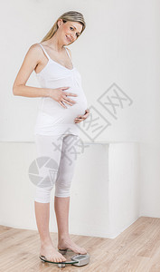 美丽的孕妇站在体重秤上图片