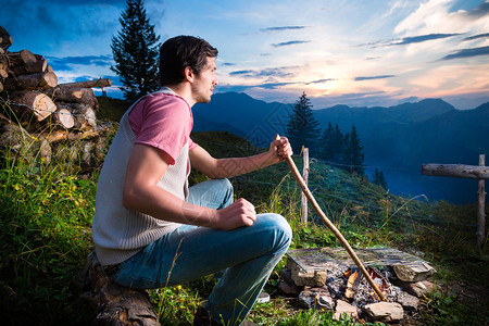 坐在巴伐利亚阿尔卑斯山脉营火上山顶高山草原上的年轻人图片
