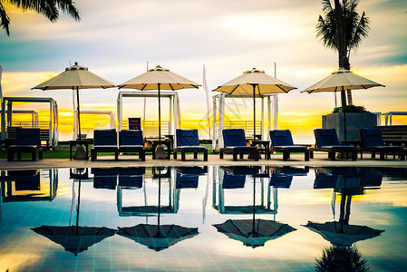 日出时在豪华酒店度假胜地配有雨伞和椅子的棕榈树纸影带棕图片