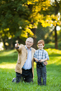 祖父和孙子在公园里通过望远镜观察图片