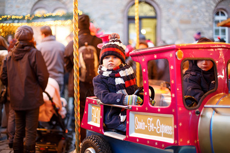 美丽的小男孩在圣诞游乐场或市场的旋转木马上图片