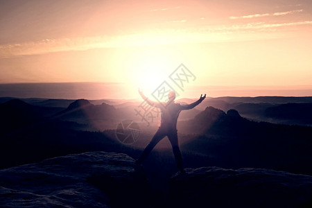 黑衣穿梭的跳跃健行者庆祝两个岩石峰之间的胜利图片