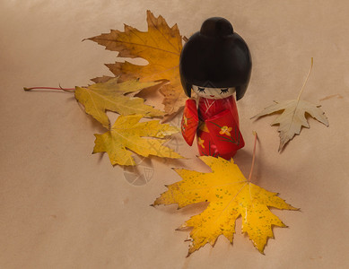 棕色背景的日本传统洋娃木Kokeshi和黄色树叶图片