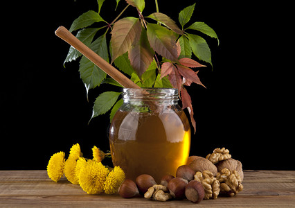 黑色背景中的蜂蜜罐黄色花朵坚果和秋叶图片