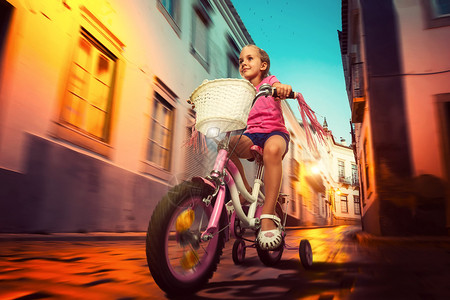 晚上在街上骑粉红色自行车的微笑小女孩图片