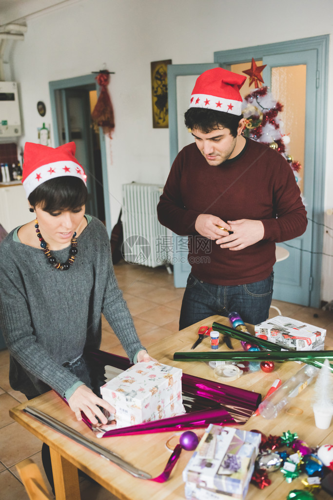 年轻英俊的白人男女夫妇用包装纸和丝带包裹圣诞礼物的膝盖形象图片