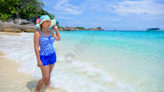 美丽的女人穿着蓝色条纹泳衣和帽子站在海边的沙滩上图片