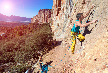 男女登山者小组以绳索和渔具攀爬橙色亮岩壁图片