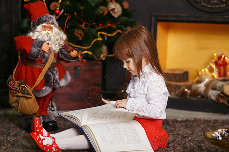 小女孩坐在美丽的圣诞装饰品的地板上读童话玩具圣诞老人的女孩女孩玩图片