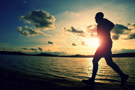运动活跃男子在日落时在海滩上跑步图片
