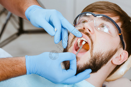 检查并选择牙医椅上牙齿的颜色牙医制作男患图片