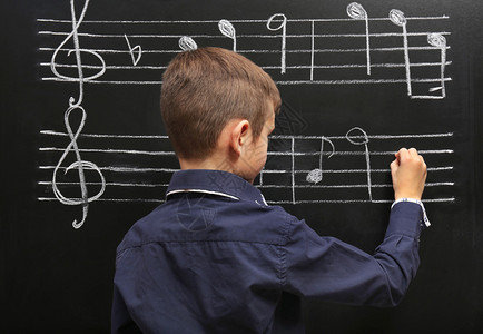 可爱男孩在黑板上写音乐笔记图片