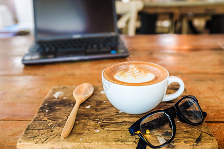 深色木桌上的一杯拿铁艺术咖啡和笔记本电脑图片