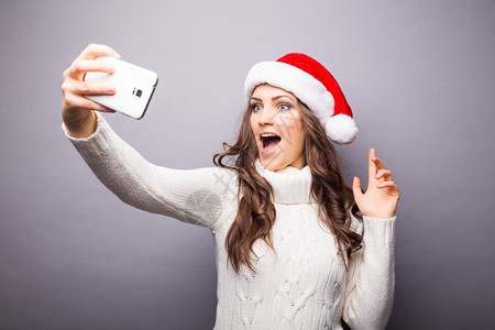 美丽的女孩的圣诞肖像戴着圣诞老人帽子的女孩女孩在手机图片