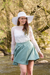 穿着时髦的帽子和在小溪户外摆布的漂亮时尚女郎图片
