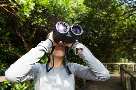 亚洲青年妇女在森林使用望远镜的图片