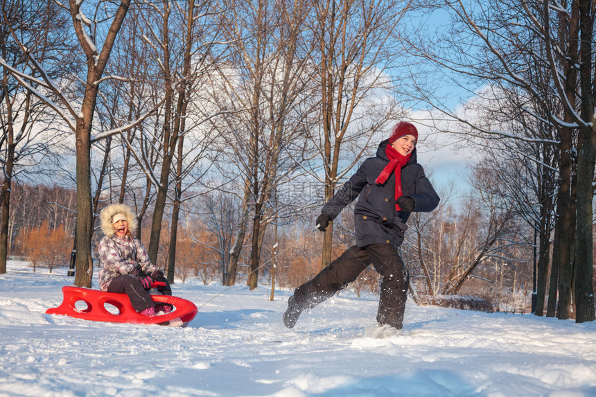 快乐的男孩和女孩一起在下雪的冬季公园玩耍男孩用红色塑料图片