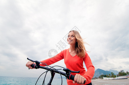 美丽的年轻女子在海边行走骑着自行车对抗阴图片