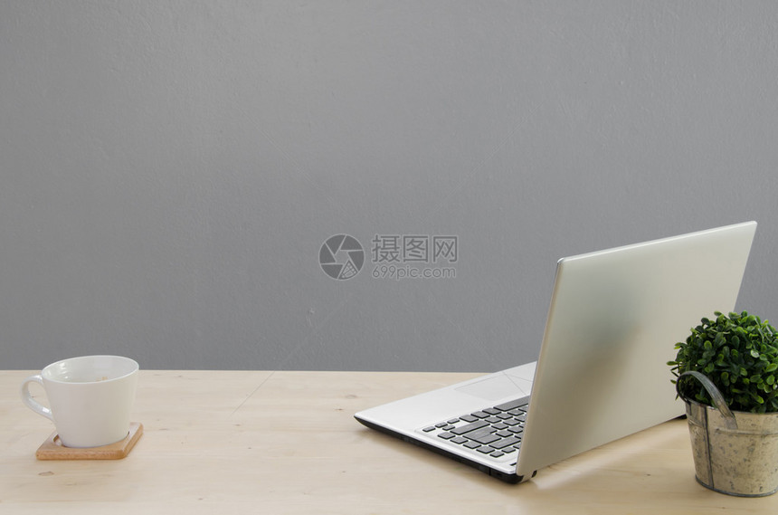 用笔记本屏幕的办公桌篮子上的绿树和白咖啡杯从前面看图片