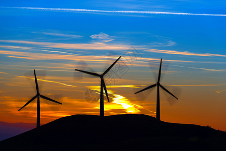 山中风力涡轮机的三个剪影与美丽的日落图片