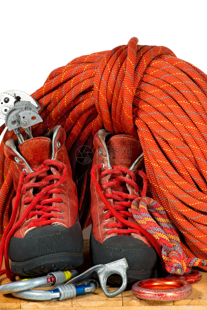 带有登山靴登山凸轮下降器登山扣岩钉和红绳的攀岩设备在白图片