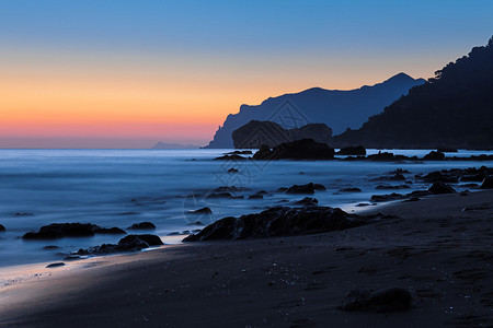 岩石海滩上的戏剧海岸日落低快门速度图片