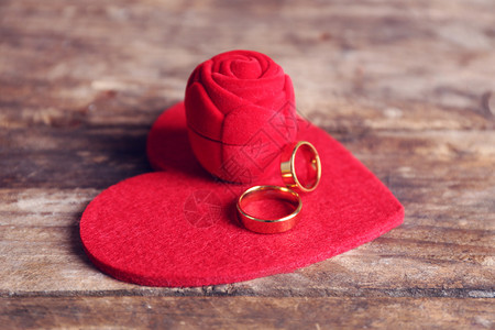 红丝织绸玫瑰盒和婚礼戒指用心在木背景图片