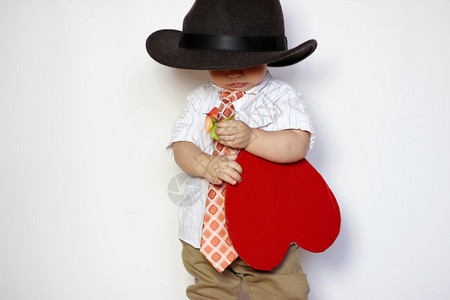 戴着帽子和领带的小男孩拿着红纸心图片