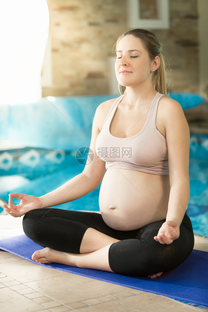 年轻平静的孕妇在游泳池打坐图片