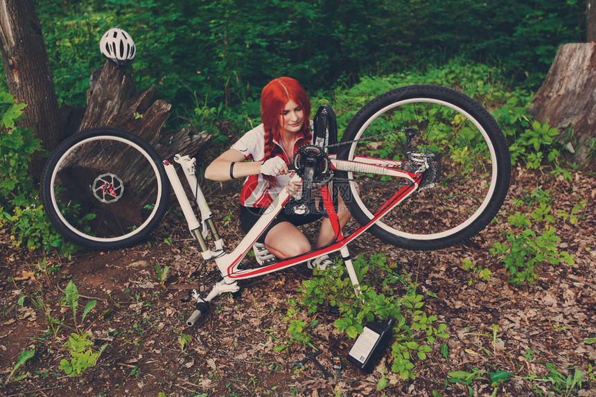 年轻的运动女自行车手或女运动员在森林里修理她的m图片