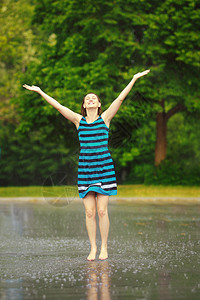 穿着蓝色连衣裙的快乐年轻白人女孩在雷雨中跳水坑的肖像图片