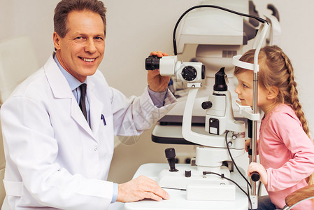 英俊眼科医生用现代设备和笑容检查小女孩眼睛图片