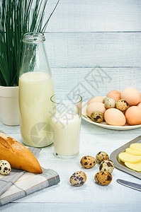 白木背景上的牛奶瓶玻璃鸡蛋黄油和面包图片