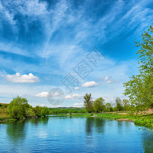 从绿树和蓝天多云的河岸看图片