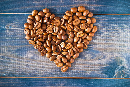 蓝色木质背景上由咖啡豆制成的心形图片