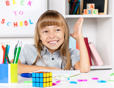 快乐的小女孩坐在教室的书桌上做功课图片