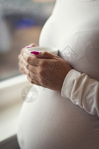 一位深思熟虑的孕妇在窗外看家喝茶或咖啡心理健康和怀孕精神健图片