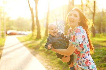 美丽的年轻女子与男婴孩子男孩站在夏天日落的草地上公园里的幸福家庭户外图片