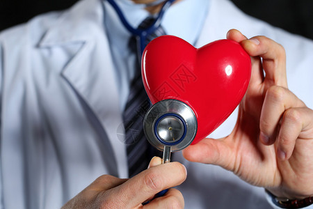 男医学生手持红色玩具心脏和听诊器特写黑色背景图片