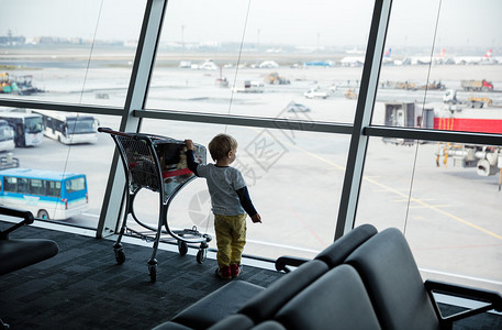 小男孩站在机场的窗户边看着陆场图片