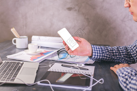 Sideview的男与空白的色智能手机在手坐在办公桌与业务报告和电图片
