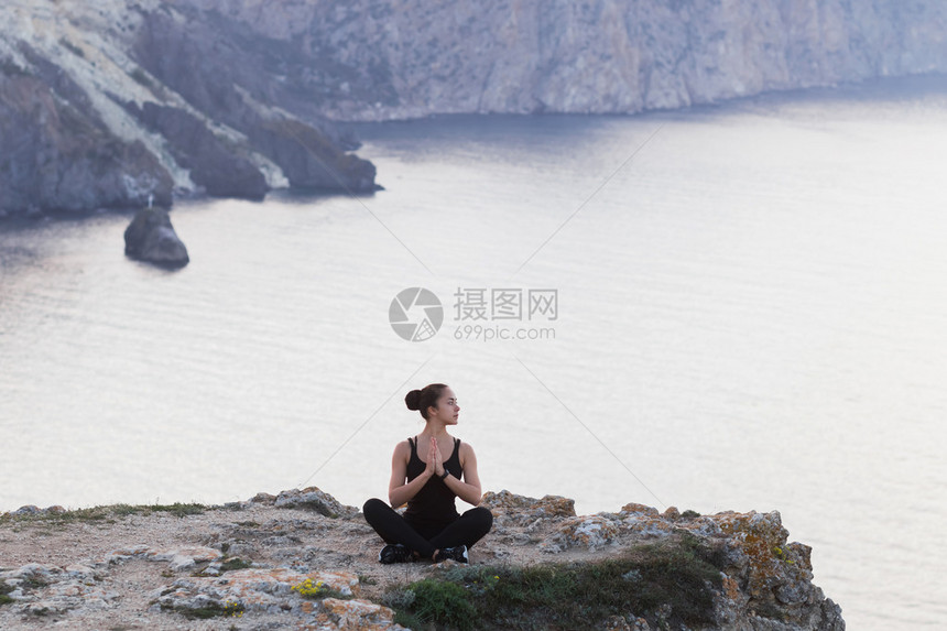 女人在悬崖边上练习瑜伽姿势迎接日出图片