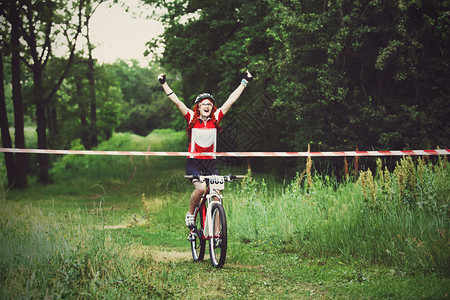 优胜者胜利时刻戴着防护头盔的年轻红发女自行车手越过终点线图片