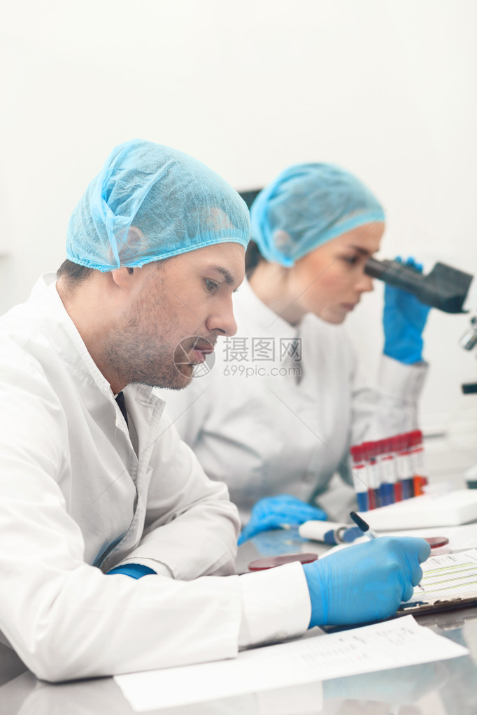两名有技能的科学家正在进行调查男人正集中地坐着写作女人正在用显微镜分析样图片