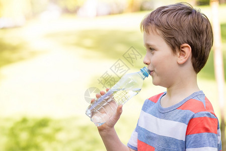 可爱的小男孩喝矿泉水从公园的塑图片