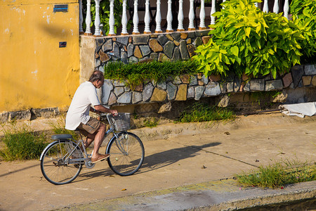 老人骑着自行车在沥青路上行驶走向阳图片