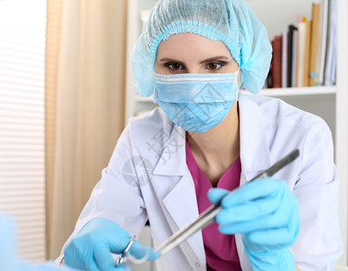 戴着面具的漂亮女外科医生在缝合伤口时拿着针镊子和镊子图片
