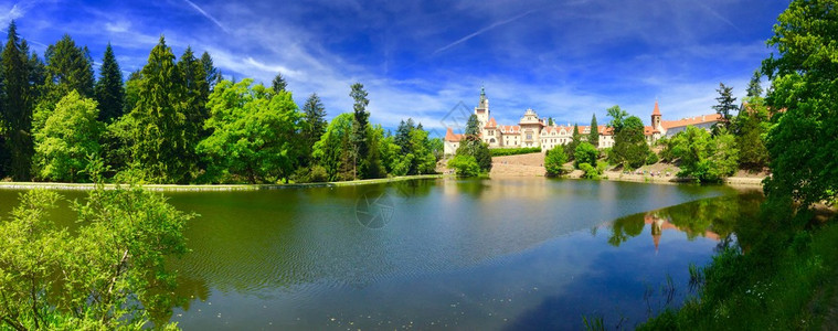美丽城堡的全景其自然湖泊在深森林与蓝天图片