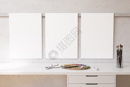 白色桌面上方有油漆调色板管子和刷子的混凝土墙上挂着三个空白图片
