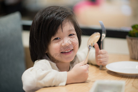 亚洲可爱儿童在餐馆里拿着一勺子和图片